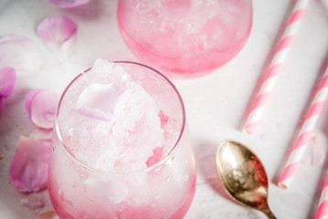 Summer refreshing desserts. Vegan diet food. Ice cream frozen rose, froze, with rose petals and rose wine. On a white concrete table, with spoons, striped straws, petals and rose flowers. Copy space