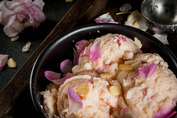 Summer refreshing desserts. Vegan diet food. Ice cream with rose petals and slices of almonds, on wooden old tray, on black stone table. With spoon for ice cream and ingredients. Close view
