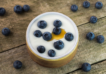 White yogurt in ceramic bowl with blueberries and honey on rustic wood.