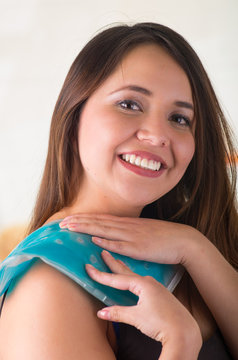 Close up of a beautiful smiling woman holding ice gel pack on her shoulder, medical concept, in office background