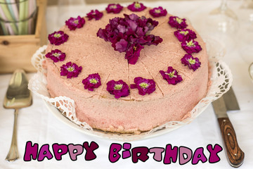 Close up cream cake violet flowers on top silverware and colorful text happy birthday