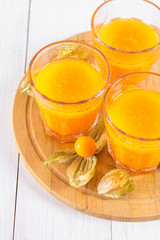 An orange smoothie made of physalis on a white wooden table.