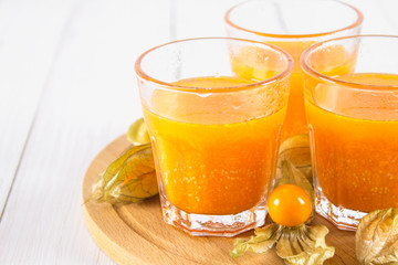 An orange smoothie made of physalis on a white wooden table.