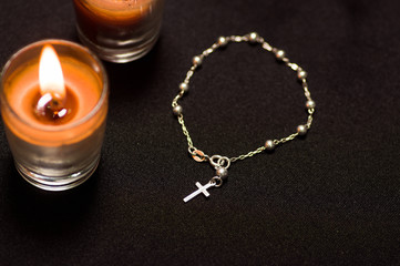 Fototapeta na wymiar Rosary beads with an orange candle in black background, above view