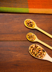 Wooden spoons with toasted corn grains, known as tostado in south america, spread around bowl containing yellow salsa, seen from above