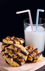 Cookies with peanuts covered with chocolate icing, and a glass of milk on a dark wooden background.