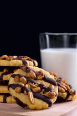 Cookies with peanuts covered with chocolate icing, and a glass of milk on a dark wooden background.