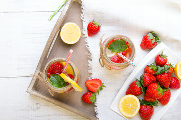 Mineral  water with fresh strawberries, lemon  and mint in jar on a white wooden background, copy space