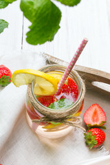Mineral  water with fresh strawberries, lemon  and mint in jar on a white wooden background, copy space
