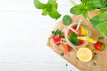 Mineral  water with fresh strawberries, lemon  and mint in jar on a white wooden background, copy space