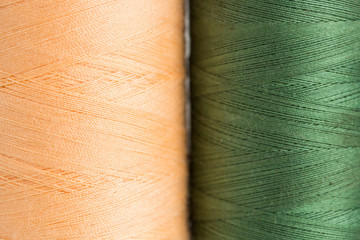 sewing, patchwork and tailoring concept - close-up on apricot or peach and green color threads in new bobbins at workshop, macro of quilting tools preparations