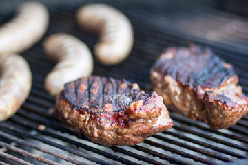 steaks and brauts cooking outdoors on flaming grill