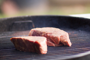 Raw steaks cooking outdoors on flaming grill