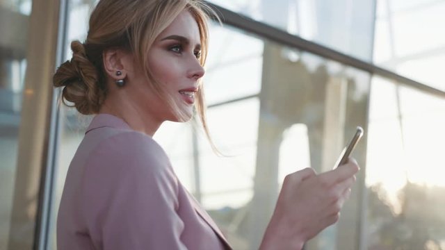 Rotation view of an elegant blonde business lady using her phone, looking around in a bright sunshine. Modern technologies, active lifestyle. Working day. Natural beauty.