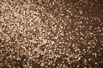 Abstract background of bronze glitter sparkling in defocused bokeh under bright light