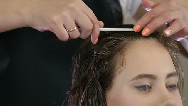 Hairdresser combing hair of teen girl client in hair salon