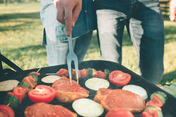Friends making barbecue and having lunch in the nature. Couple having fun while eating and drinking at a pic-nic - Happy people at bbq party