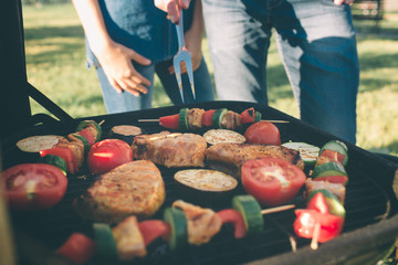 Friends making barbecue and having lunch in the nature. Couple having fun while eating and drinking at a pic-nic - Happy people at bbq party