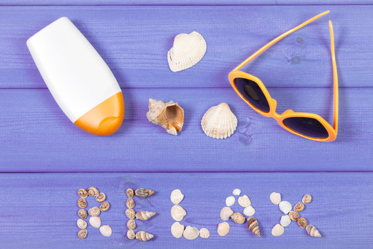 Word relax made of seashells, sunglasses and sun lotion on boards, concept of summer time