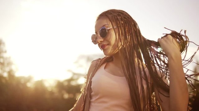 Young beautiful girl with dreads dancing in a park. Beautiful woman in jeans and sunglasses listening to music and dancing during a sunny day. Slowmotion shot.