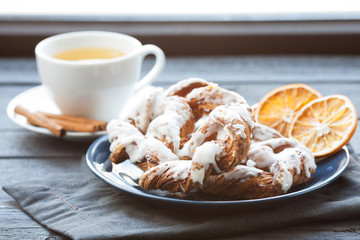 Bavarian cream puff with crushed hazelnut and lemon fondant on a blue plate. In the background, green tea with cinnamon sticks