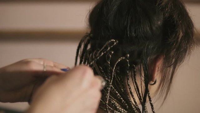 Closeup view of the hairdresser's hands doing dreads for a young woman in the hair salon. Slowmotion shot