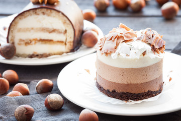 Mousse cake three chocolate and cake sour cream whole hazelnut and cinnamon sticks on a white plate. Dark wooden background