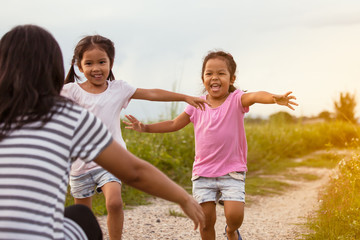 Two asian little girls running to their mother to give a hug in the park in vintage color tone