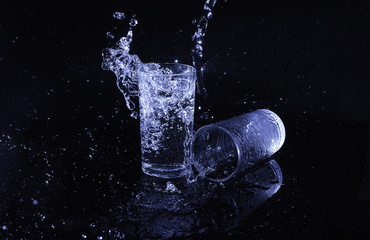 water splashing out of a glass with droplets frozen in motion against a dark background, creating a dramatic and refreshing visual effect.