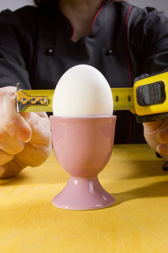 Egg in holder and hands with tape measure
