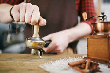 Closeup shot of barista working in coffee shop: pressing fresh grains with tamper after grinding them in antique mill
