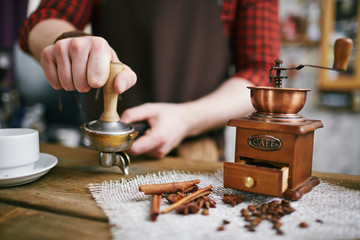 Closeup shot of barista working in retro coffee shop: pressing fresh grains with tamper after...