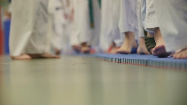 A lot of teenagers karatekas in white kimono going on tatami - legs close up