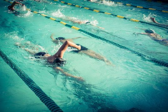Close-up action shot of teen boy swimming front crawl stroke style in the blue water outdoor race pool. Focus on arm and water splash, some motion blurs. Swimming race and competition concept. Vintage
