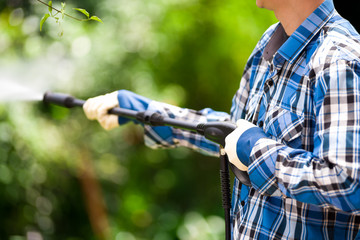 Young man wearing square pattern blue holding high pressure water gun, on a garden background