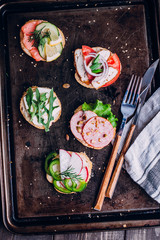 Crostini with different toppings on black table background. Delicious appetizers. Brushetta snacks for wine. Variety of small sandwiches with vegetables, top view