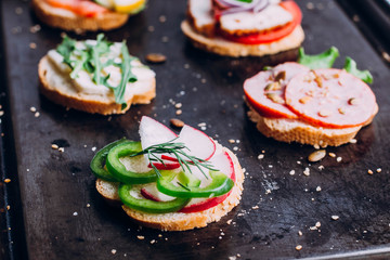 Crostini with different toppings on black table background. Delicious appetizers. Brushetta snacks for wine. Variety of small sandwiches with vegetables, top view