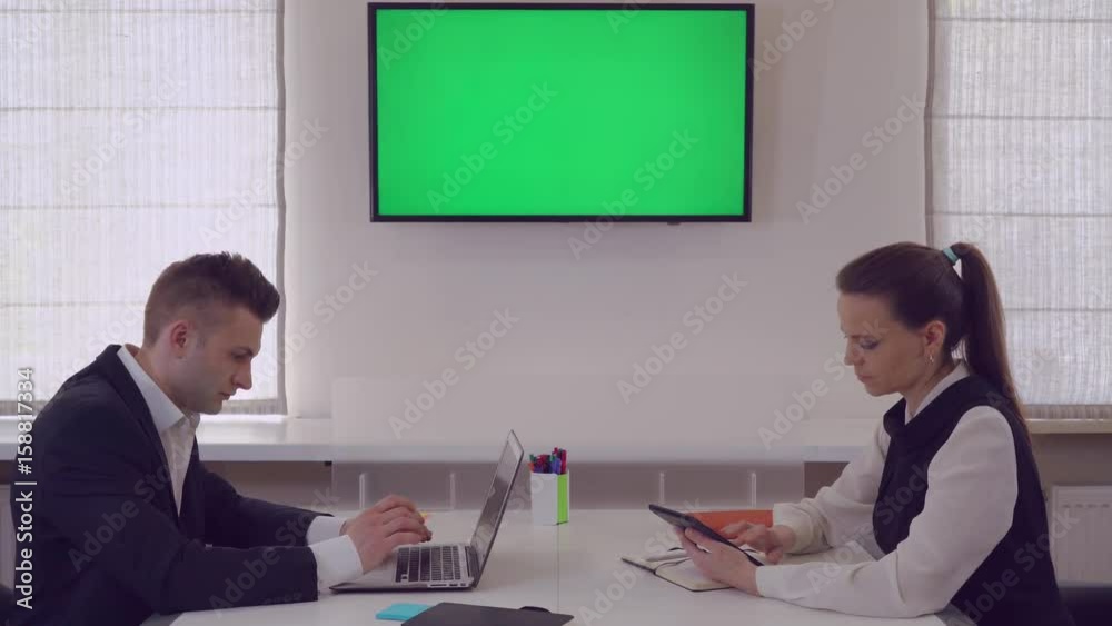 Poster Managers focused at work finalizing presentation. Co workers sitting in boardroom using laptop. Two adult workers in office wearing elegant suit.
