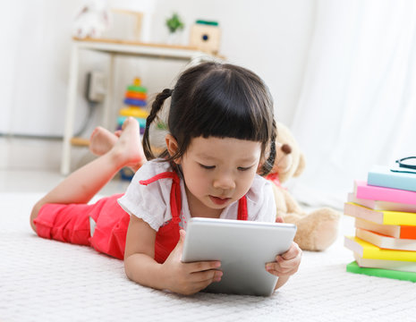 Preschooler girl plaing tablet. Cute child reading with teddy bear. Little girl having fun indoors at home, kindergarten or