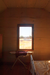 Abandoned room in Australian ghost town with iron board in old house, view through window with dry outback landscape in background.