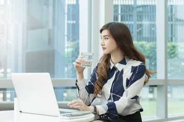 Cute asian woman drinking water at modern office workplace. Professional business woman relax from work.