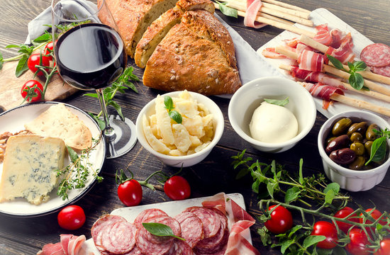 Different meat and cheese products with red wine on dark wooden table
