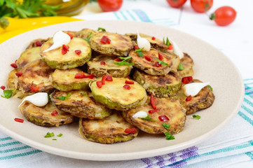 Spicy salad of fried slices of zucchini and young garlic, spices, herbs and red pepper on a plate on a white wooden background. Close up
