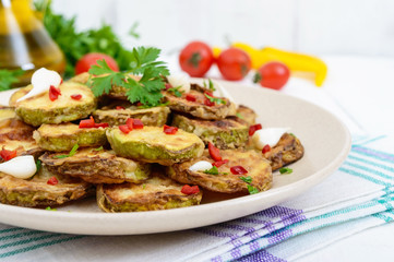 Spicy salad of fried slices of zucchini and young garlic, spices, herbs and red pepper on a plate on a white wooden background.