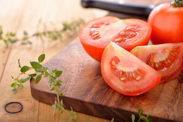 whole and portion cut fresh tomato with herb on cutting board - obrazy, fototapety, plakaty
