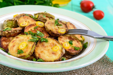 Fried slices of young zucchini with hot pepper, greens on a plate on a wooden background. Close up. Vegetarian cuisine. Vegetable dish.