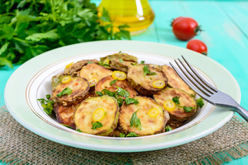 Fried slices of young zucchini with hot pepper, greens on a plate on a wooden background. Vegetarian cuisine. Vegetable dish.