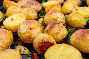 Baked potatoes with a golden crust on a black background with hot pepper, garlic, spices and herbs. Close-up.