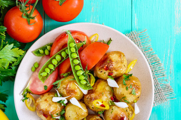 Spicy salad of baked potatoes, young garlic, tomatoes, green peas on a plate on a bright background. Top view. Close up