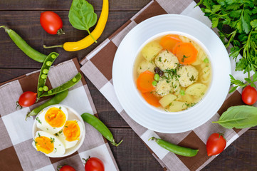 Light dietary soup with meat balls, vegetables, fusilli and boiled eggs on a dark wooden table. Top view. Useful lunch.